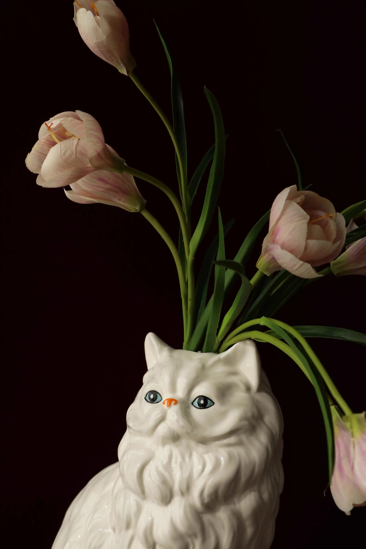 A white ceramic cat sculpture with pink tulips emerging from its head.