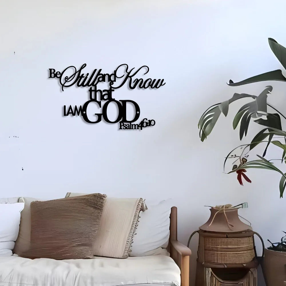 A minimalist metal wall sign featuring the text Be Still and Know that I am God with a palm of olive branch.