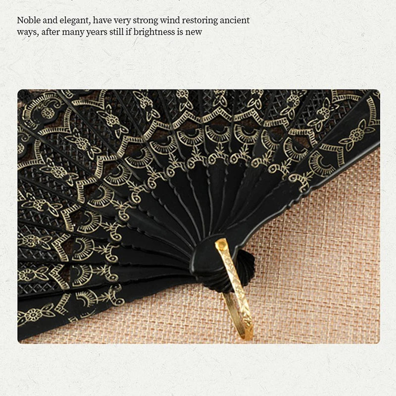 A close-up of an elegant black lace folding hand fan with gold accents resting on a beige fabric.