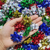 A hand holds a collection of holographic and glittery star gift bows in various colors like red, blue, green, and gold.
