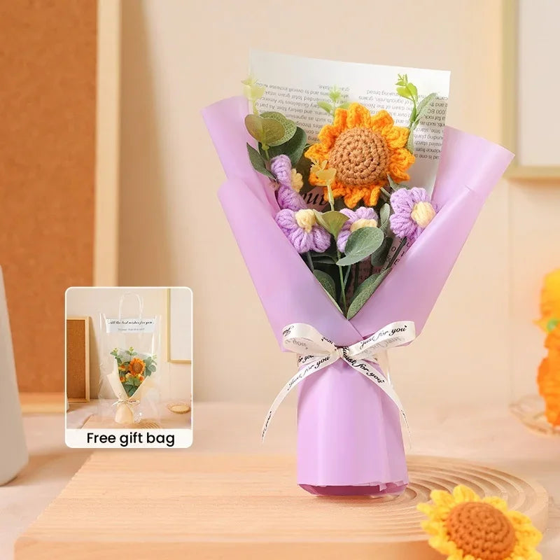 A purple bouquet of handcrafted crochet sunflowers and purple flowers tied with a white ribbon in a gift bag.