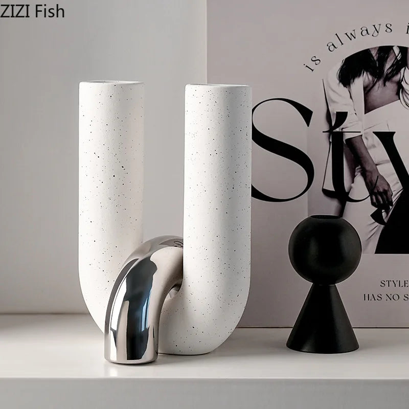 White ceramic U-shaped tabletop vase and black spherical sculpture displayed on a white shelf.