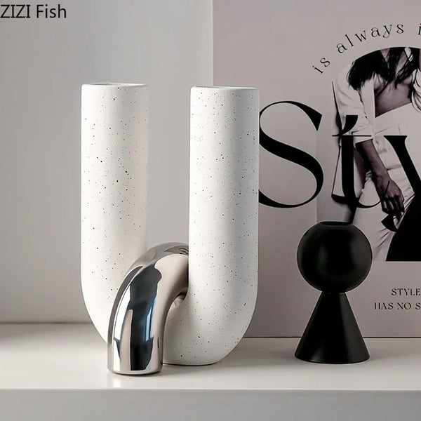 White ceramic U-shaped tabletop vase and black spherical sculpture displayed on a white shelf.