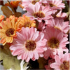 A close-up of three pink and orange silk gerbera daisy artificial flowers with dark centers.