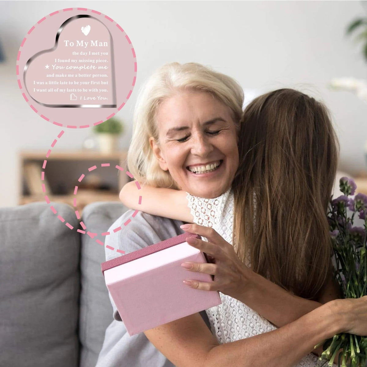A woman is hugging a man while holding a pink acrylic heart keepsake plaque with a message to him.