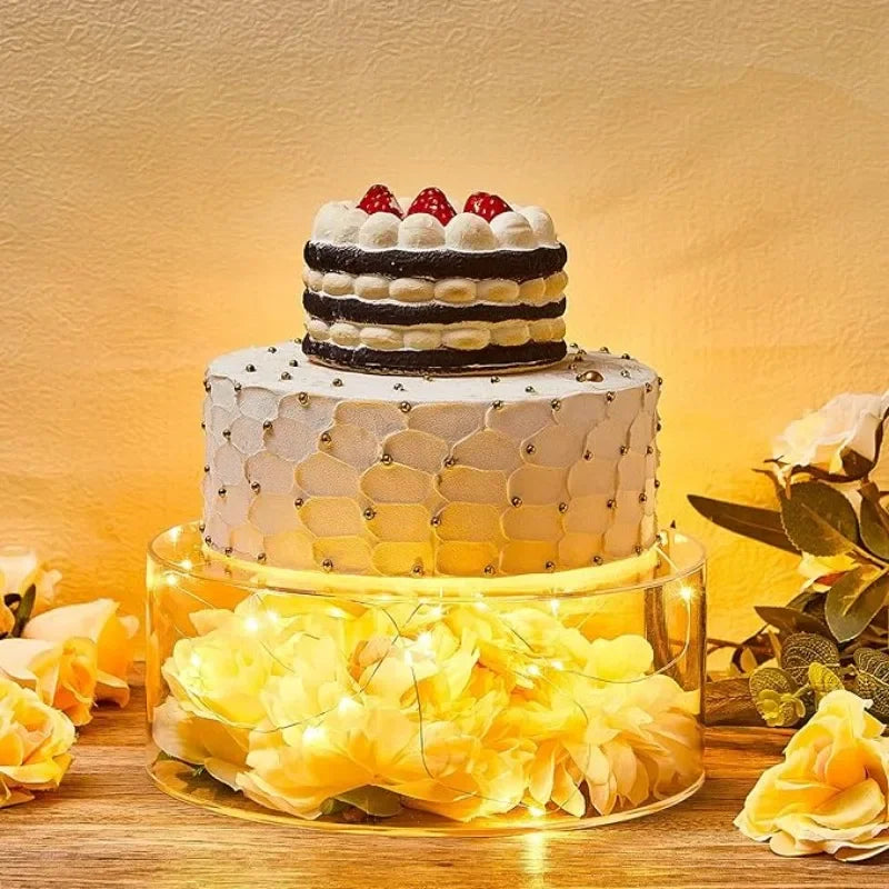 A tiered white cake decorated with black stripes and gold accents displayed on a clear acrylic stand.