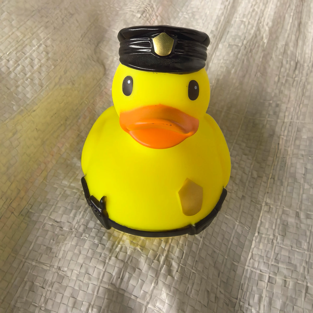 A yellow rubber duck bath toy with a black cap and orange beak resting on a silver-textured surface.