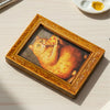 A wooden framed picture of an orange cat looking at the viewer.