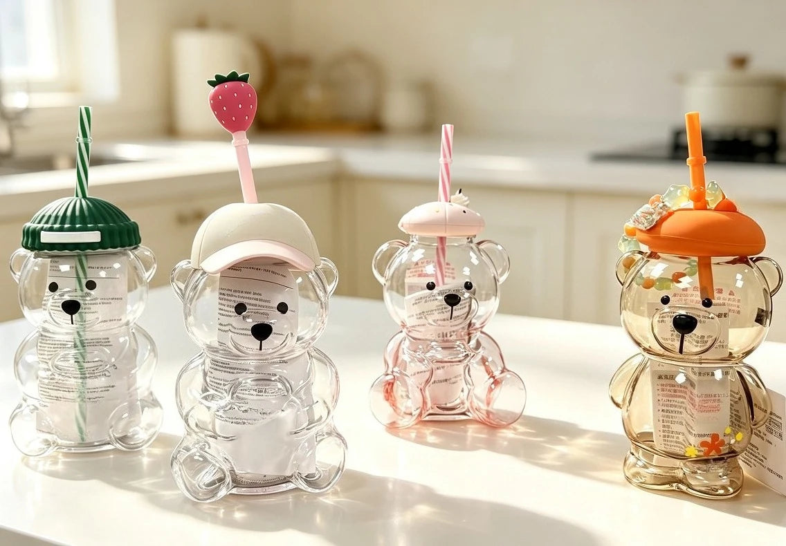A collection of clear glass coffee cups shaped like bears with pink and orange straws on a white table.