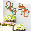 Handcrafted metal gecko wall art featuring colorful, stylized geckos mounted on a white wooden panel.