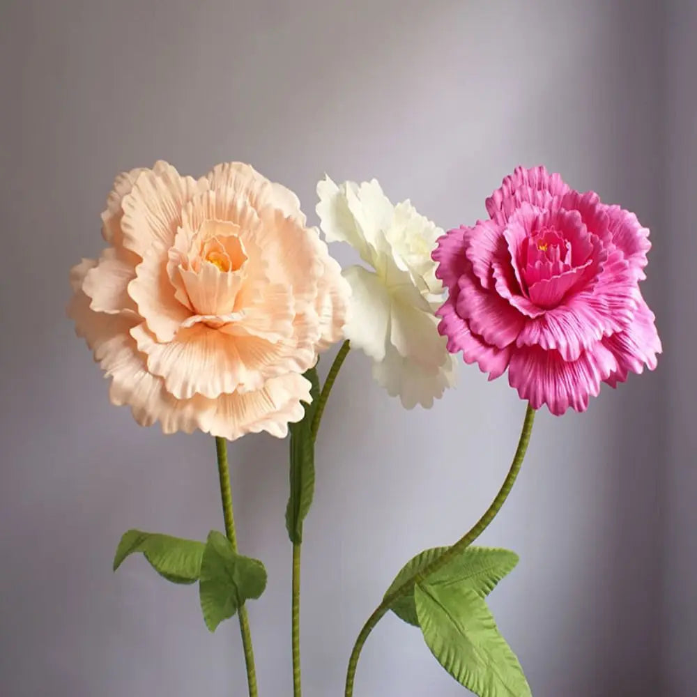 Three silk foam roses in peach, cream, and pink bloom on green stems against a gray background.