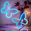 A bright blue neon sign shaped like a butterfly is displayed on a wooden surface with a potted plant in the background.