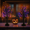 A glowing Halloween birch tree lamp with LED lights sits on a wooden table next to an orange jack-o'-lantern.