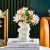 A white Nordic spiral decorative vase filled with pink and white flowers sits on a book.