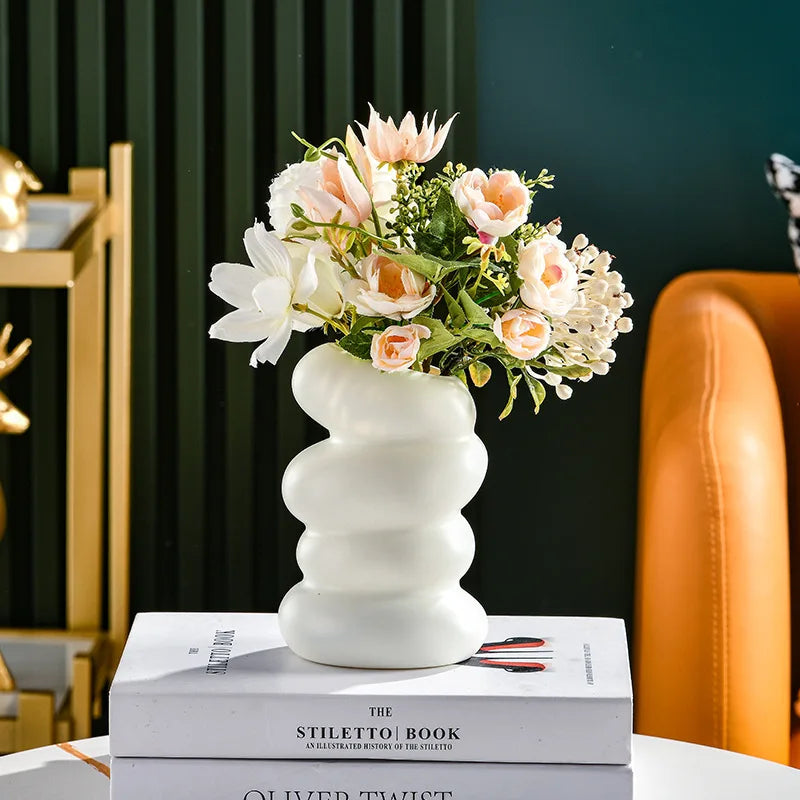 A white Nordic spiral decorative vase filled with pink and white flowers sits on a book.