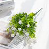 A branch of artificial eucalyptus with seven stems, featuring bright green faux leaves and white flowers.