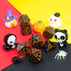 A set of seven polyhedral dice including a witch hat, pumpkin, and skull figures displayed on a red and yellow background.