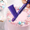 A hand holds a purple pearl ball applicator tool used for decorating fondant and cake surfaces.