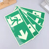 A stack of photoluminescent emergency exit sign decals in green and white on a light gray surface.