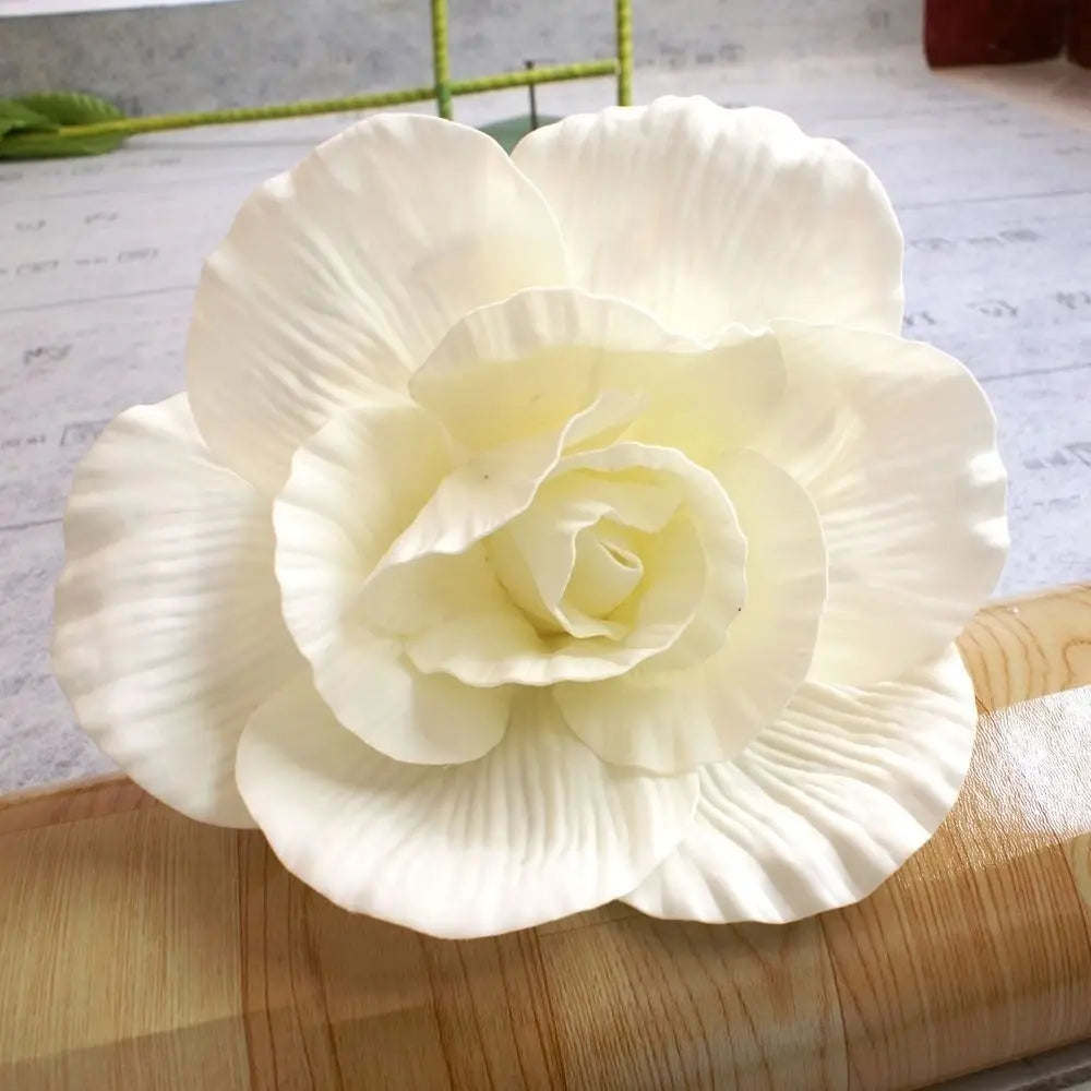 A white silk foam rose flower with layered petals resting on a wooden cutting board.