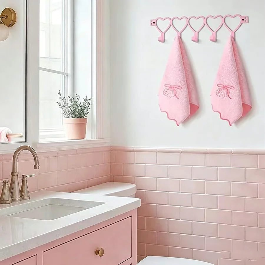A pink heart over-the-door hook rack with five pink fabric hooks displayed on a white wall above a pink tiled vanity.