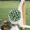 A large sphere of white artificial roses displayed on a wooden stand in an outdoor setting.