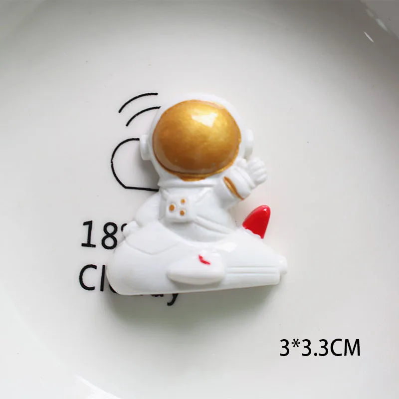 Décoration de gâteau miniature d'astronaute blanc avec un casque doré sur une assiette blanche.