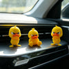 Three yellow 3D printed angry duck statues sitting on a car dashboard.