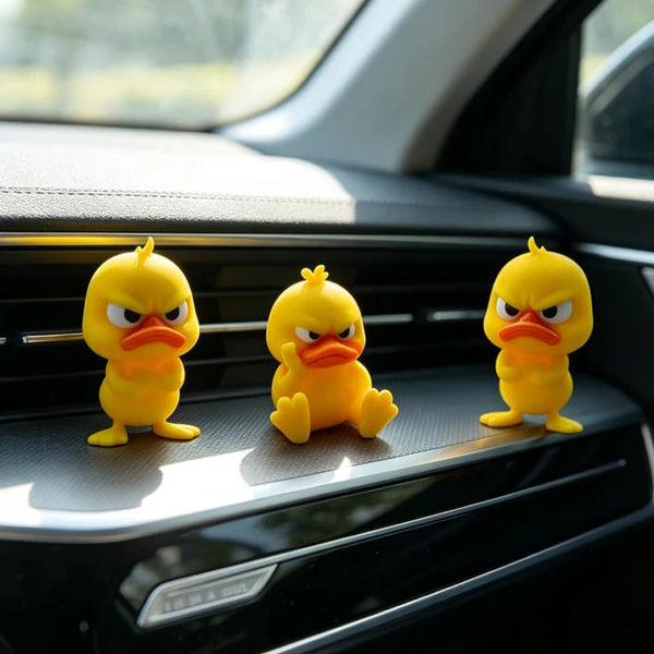 Three yellow 3D printed angry duck statues sitting on a car dashboard.