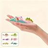 A hand holds several colorful dinosaur slingshot flying toys for kids' party favors and prizes.