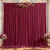 A deep burgundy fabric backdrop with gathered pleats and decorated with floral arrangements for an event.