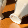 A close-up of an elegant cream ceramic vase with a smooth finish, casting a shadow on a wooden surface.