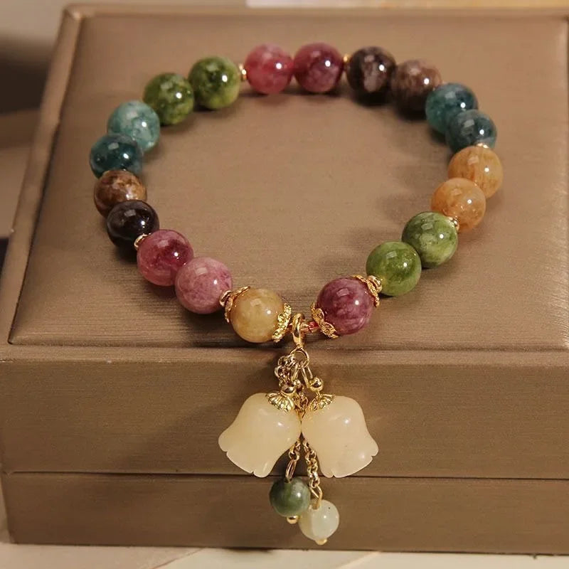 A bracelet made of various colored natural stones, including pink, green, and brown, with a gold-toned pendant.