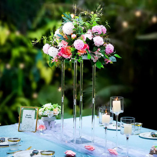 Vases de acrílico elegantes con flores rosas y blancas sobre una mesa azul claro.