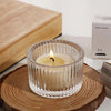 Clear glass tealight candle holder with a lit candle resting on a wooden slice.