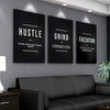 Three framed motivational canvas prints titled Hustle Grind and Execution displayed on a gray wall above a dark sofa.