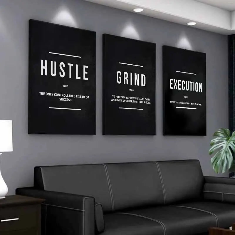 Three framed motivational canvas prints titled Hustle Grind and Execution displayed on a gray wall above a dark sofa.