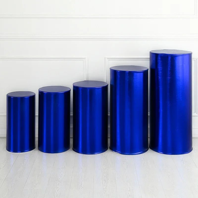 A row of six shiny blue spandex cylinder stands displayed on a white floor against a white paneled wall.