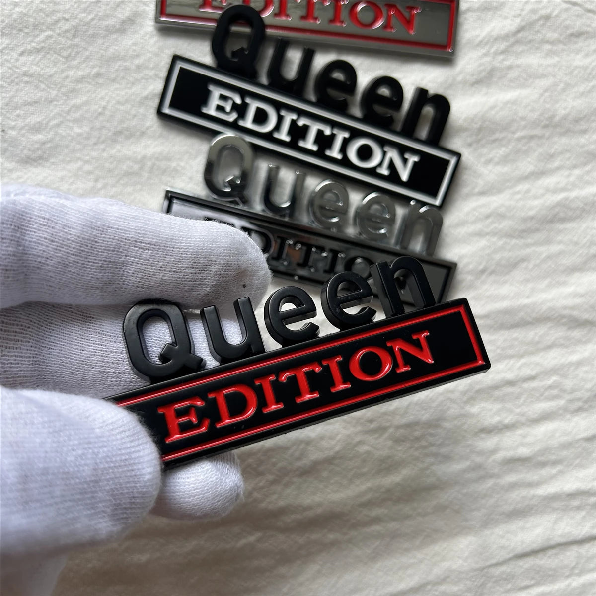 Eine Hand hält ein Set von schwarzen und roten Queen Edition Emblem-Autoklebern auf weißem Hintergrund.