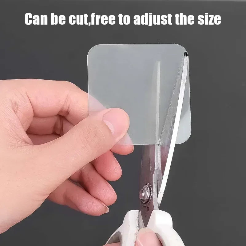 A hand is using scissors to cut a piece of clear double-sided adhesive tape, demonstrating its ability to be cut free to adju