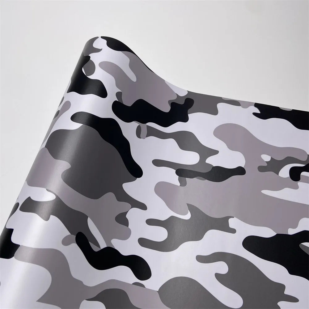 A close-up of a color-changing digital camouflage vinyl wrap film showing gray and black irregular patterns.