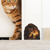 A close-up of a tabby cat looking at a small mouse figurine with a candle in a decorative niche.