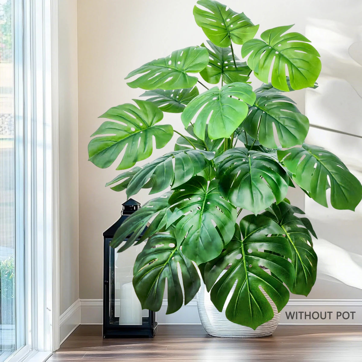 A large artificial monstera plant with green silk leaves displayed indoors near a window.