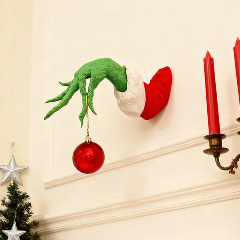 Green monster arm with a Santa hat and a red ornament hanging on a white wall