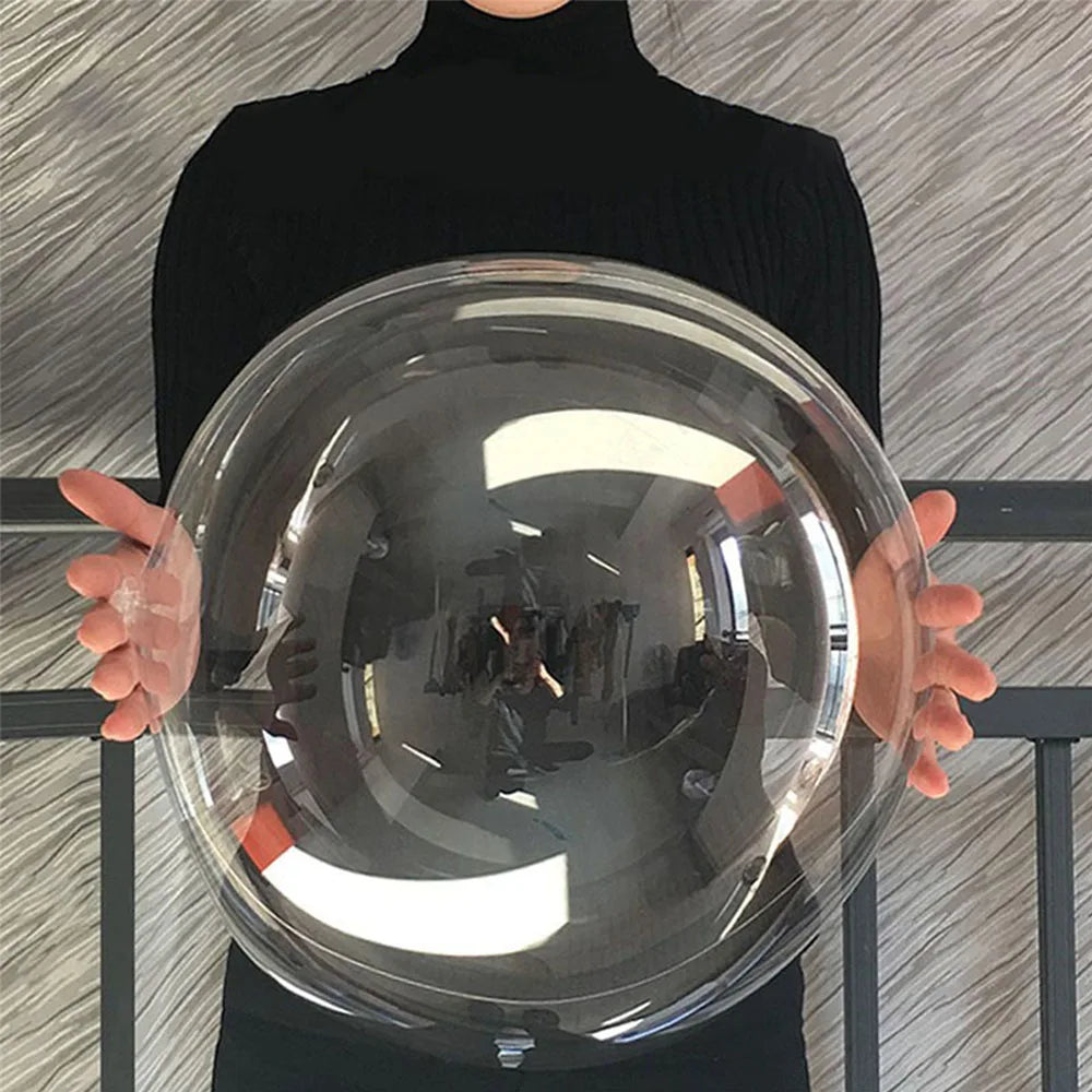A person holds a large, clear, spherical balloon reflecting light and surroundings.