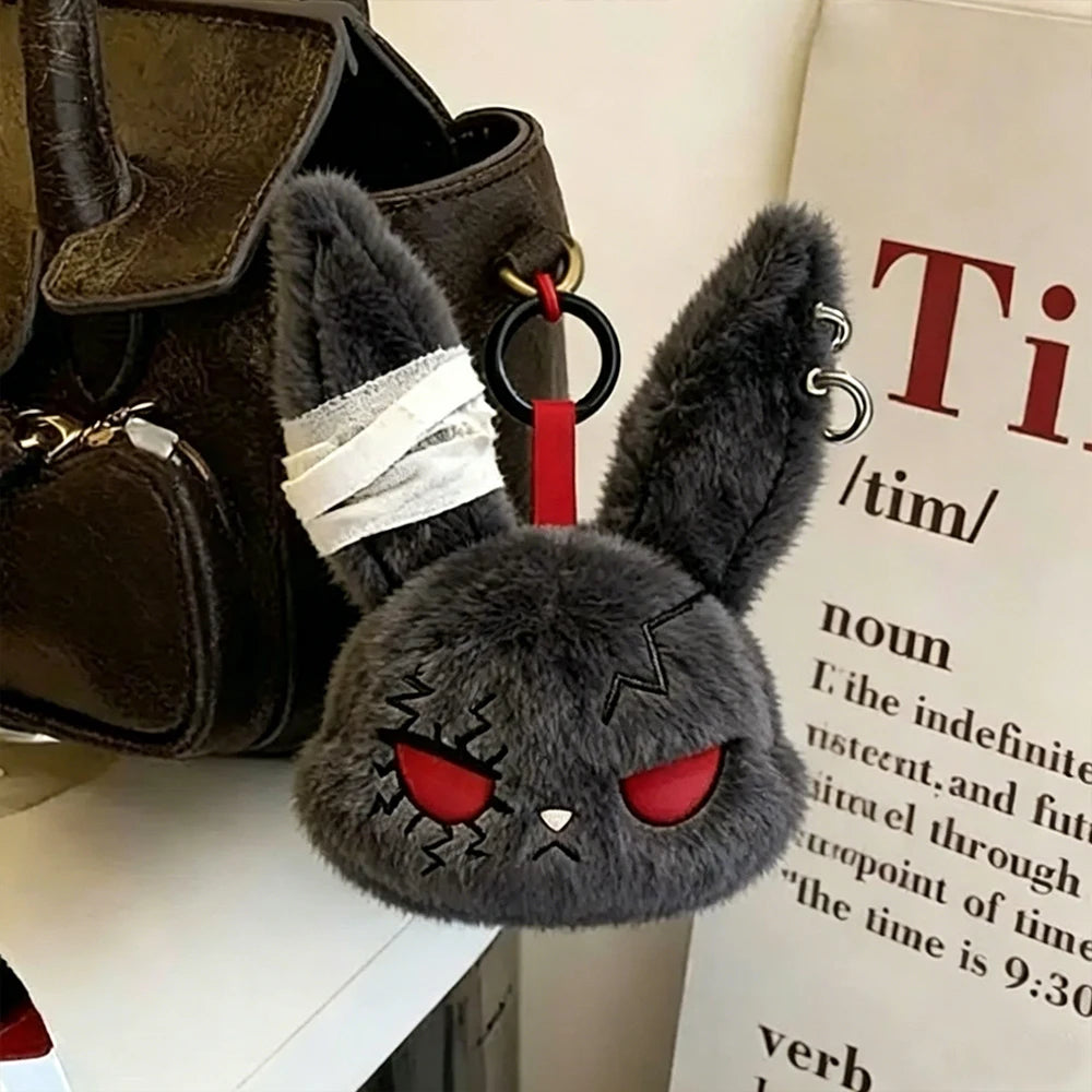 A dark gray gothic bunny plush keychain with black eyes and a white bandage design attached to a red loop.