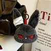 A dark gray gothic bunny plush keychain with black eyes and a white bandage design attached to a red loop.