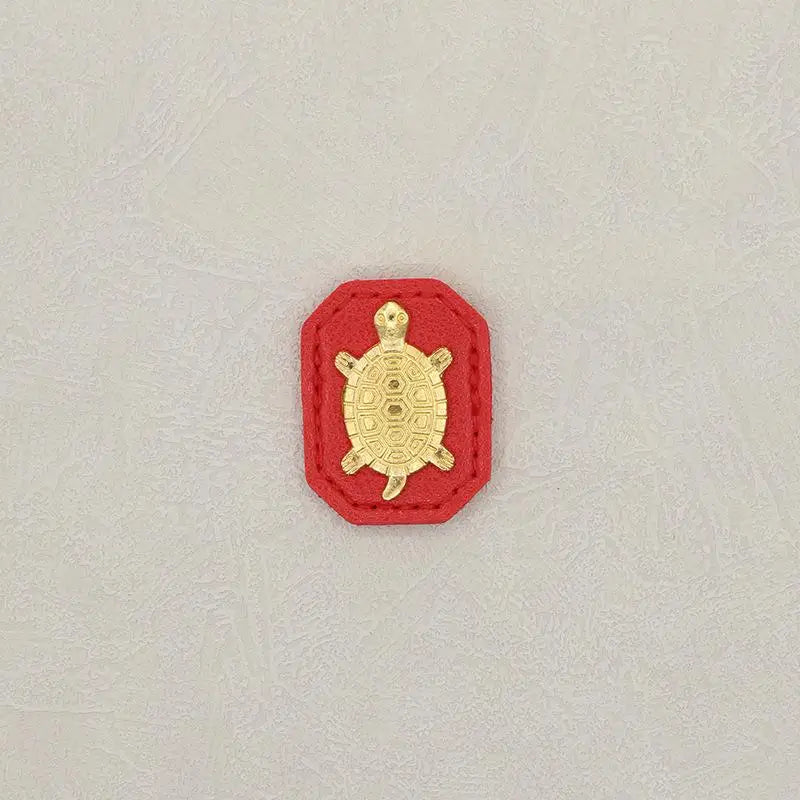 A small, gold-colored figurine of a tortoise is set against a red background.