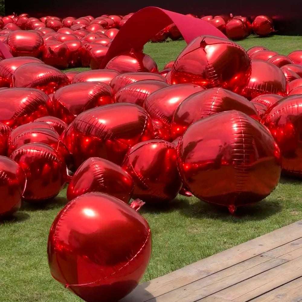 A large quantity of glossy red round foil balloons are arranged on a green lawn.