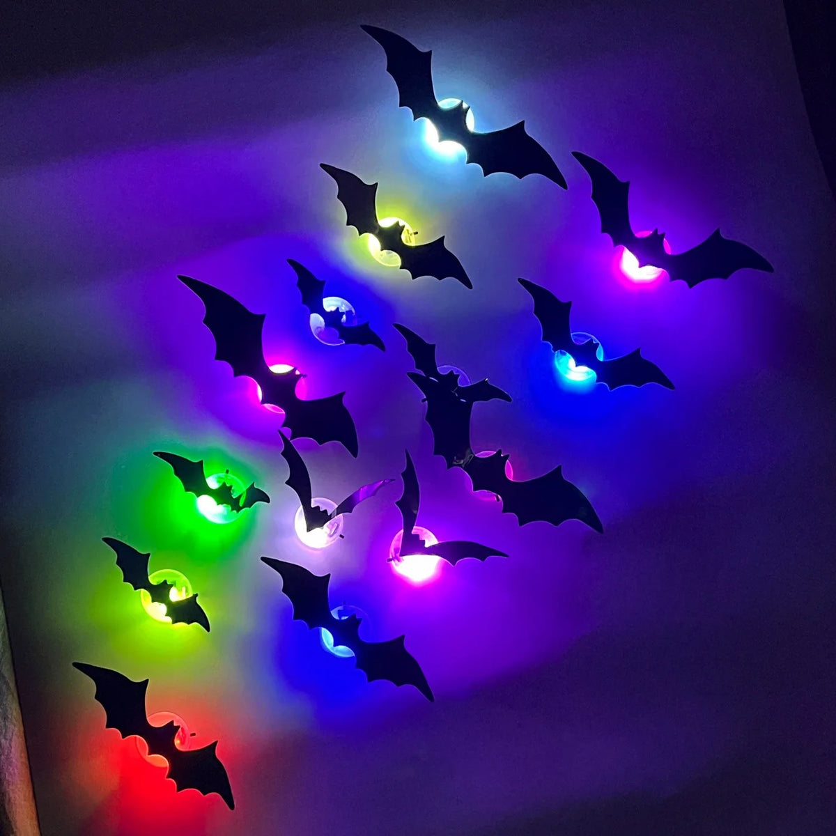 A collection of glowing black bat wall decals illuminated by colorful LED lights on a dark background.